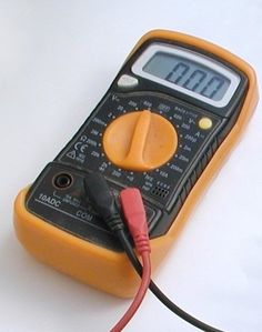 an orange and black multimeter sitting on top of a white table next to a red cord