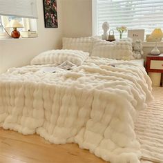 a bed covered in fluffy white blankets on top of a wooden floor