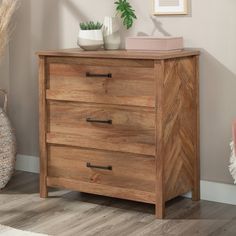 a wooden chest of drawers in a room with a pink chair and potted plant