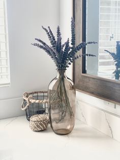 a vase filled with purple flowers sitting on top of a counter next to a mirror