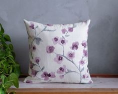 a white pillow with purple flowers on it next to a potted plant and grey wall