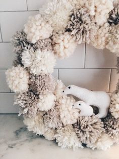 a wreath with pom - poms and a polar bear in the center on a marble countertop