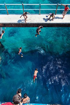 people are swimming in the blue water near a dock with a pier on one side