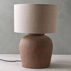 a brown table lamp with a beige shade on it's base and a black cord plugged in