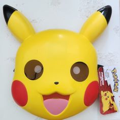 a yellow pikachu mask with brown eyes and ears is next to a candy bar