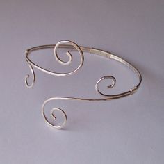 a silver cuff with two spirals on it's sides, sitting on a white surface