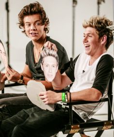 two young men sitting next to each other in chairs with one holding up a photo