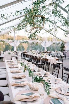 tables set up for an event under a tent with white linens and greenery