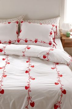 a bed with white sheets and red embroidered apples on it, along with two pillows