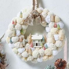 a christmas wreath with a house on it and other decorations around it, including pine cones