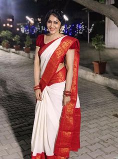 a woman in a white and red sari standing on a brick road at night