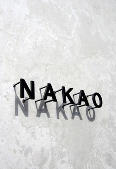 the word nakao spelled with black letters on a white wall and cement background