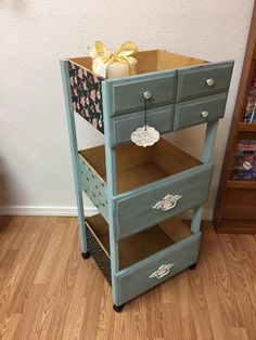 an old dresser has been painted blue and gold with flowers on the drawers, as well as a bow tied to it