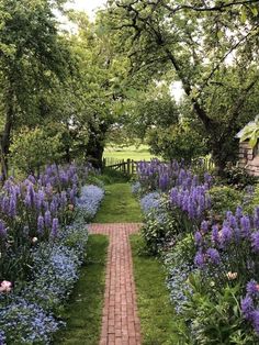a brick path in the middle of a garden with lots of purple flowers and greenery