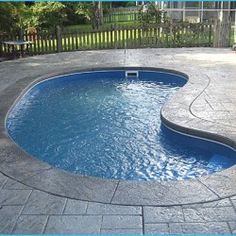 a swimming pool surrounded by a stone patio and fenced in area with an above ground hot tub