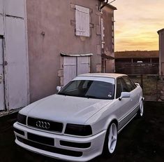 a white car parked in front of a building with the sun setting on it's side