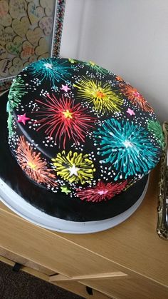 a cake with fireworks on it sitting on top of a table next to a clock