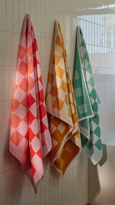 three colorful towels hanging on the wall in a bathroom with tiled walls and white tiles