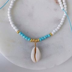 This boho chic style beaded necklace is the perfect accessory to wear to a beach brunch. The necklace features a genuine cowrie seashell wrapped with gold wire and surrounded by colored glass seed beads. The styling possibilities with this necklace are endless. Wear by itself, or layer with our other beaded necklaces! Our light blue color is the most popular to perfectly embody the ocean, but you are free to choose whatever color suits your soul. Imagine yourself walking along the beach in a flo Sea Beads Jewelry, Neckless Beads Ideas, Seashell Bead Necklace, Heishi Beads Necklace, Beach Brunch, Bubble Beads, Bracelet Business, Beaded Things, Summer Bracelet