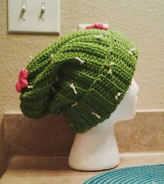 a crocheted green hat with pink flowers on it sitting on top of a white mannequin head