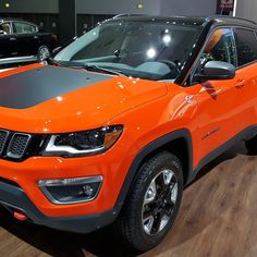 an orange jeep parked in a showroom next to two other suvs on display