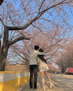 a man and woman standing next to each other on a sidewalk with cherry blossom trees in the background
