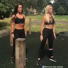 two women are doing push ups on yoga mats in a park with grass and wooden posts