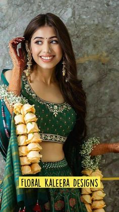 a woman in a green and gold lehenga posing for the camera with food on her hands