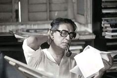 an old man sitting at a desk with a pipe in his mouth and papers around his neck