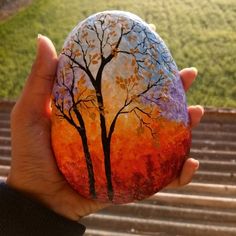 a person holding up a painted rock with trees on it in front of some steps