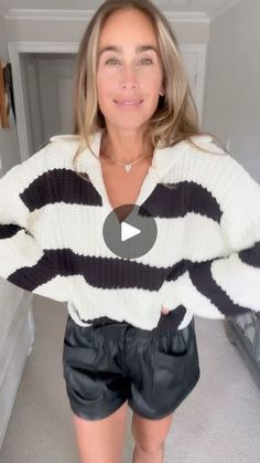 a woman wearing black leather shorts and a striped sweater is standing in front of a mirror