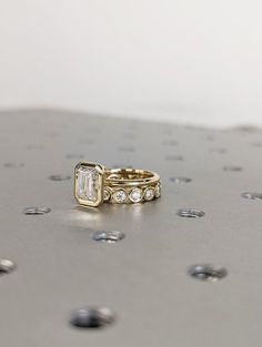 two gold wedding bands with diamonds on them sitting on a metal surface in front of dots