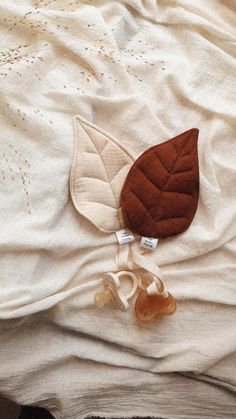 a pair of baby shoes laying on top of a white bed with a brown leaf