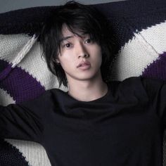 a young man laying on top of a bed next to a purple and white blanket