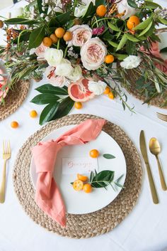 a place setting with oranges, flowers and greenery