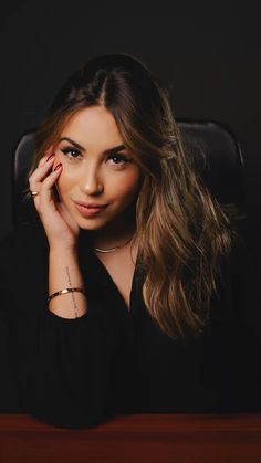 a woman sitting at a desk with her hand on her head and looking into the camera