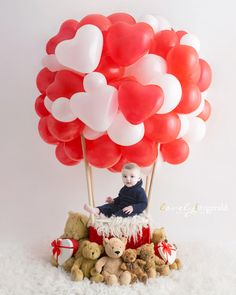 a baby sitting on top of a pile of teddy bears with balloons in the shape of hearts