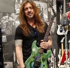 a man with long hair holding an electric guitar in front of a wall full of guitars