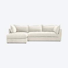 a white sectional couch with pillows on the top and bottom corner, facing away from the camera