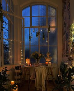 a dining room table with candles and potted plants in front of a large window