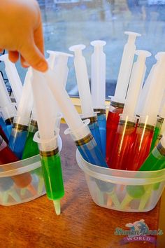 a hand is picking up some plastic straws from a container filled with colored liquids