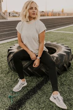 a woman sitting on top of a tire in front of an empty field with grass