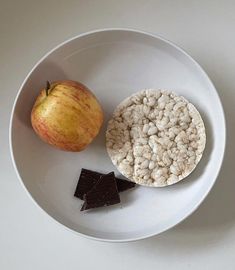 a white plate topped with cereal and an apple next to a piece of chocolate bar