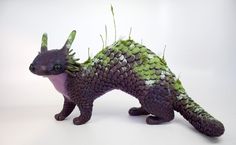 an animal made out of green and purple material on a white surface with grass sticking out of it's back