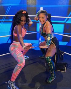 two women in colorful outfits standing next to each other on a wrestling ring with ropes
