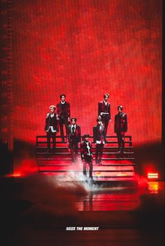 a group of men standing on top of a set of stairs in front of a red wall