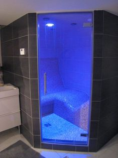 a bathroom with a blue light in the shower and grey tiles on the walls,