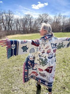 an older woman is standing in the grass with her arms spread out and wearing a scarf