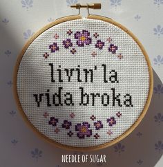 a cross stitch pattern with the words livvin la vida bronxa in black and purple flowers