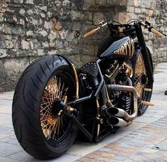 a black and gold motorcycle parked next to a brick wall on the sidewalk with its front tire missing